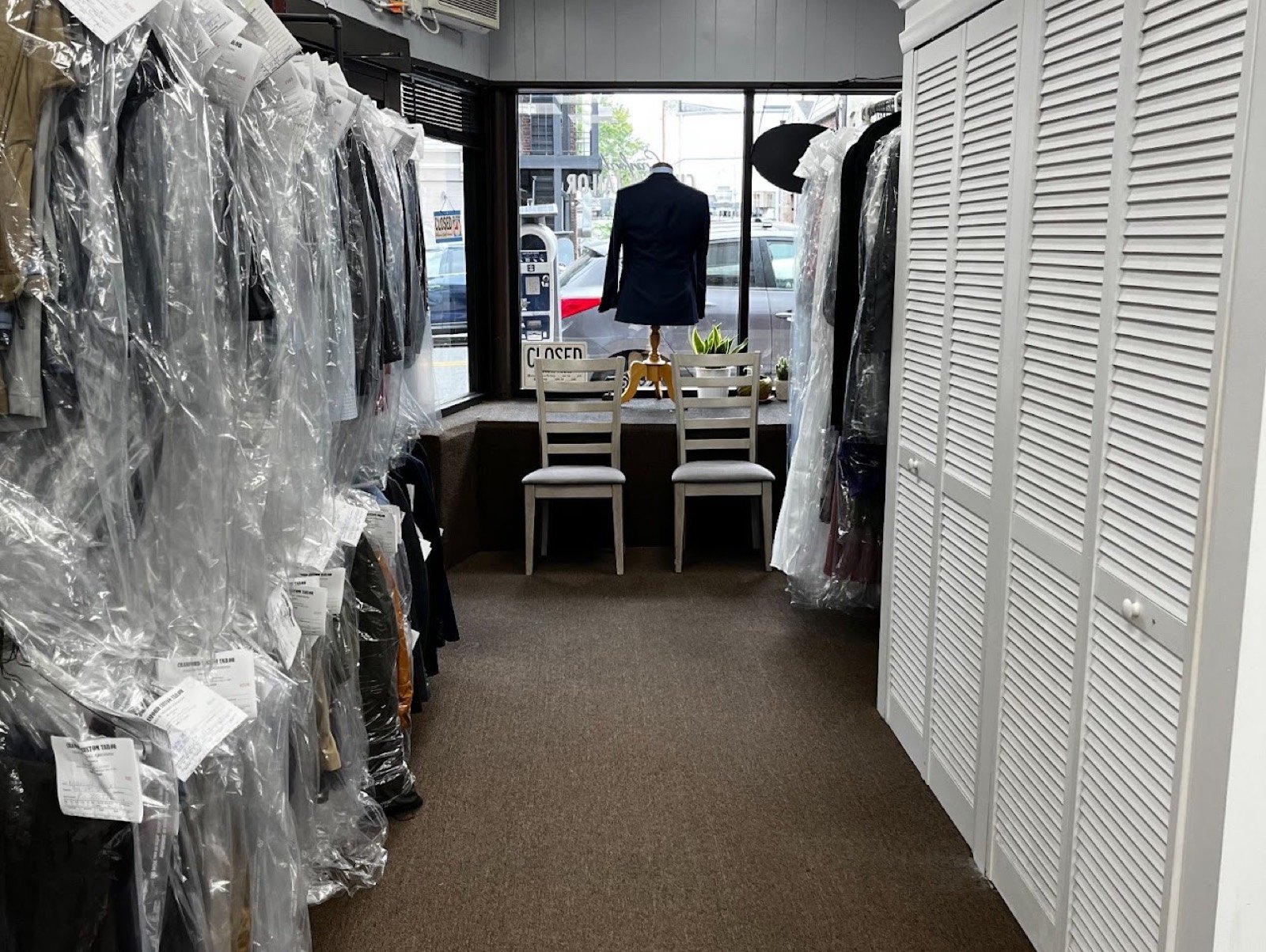 Racks of finished, tagged garments in plastic leading to the front window with a suit on display